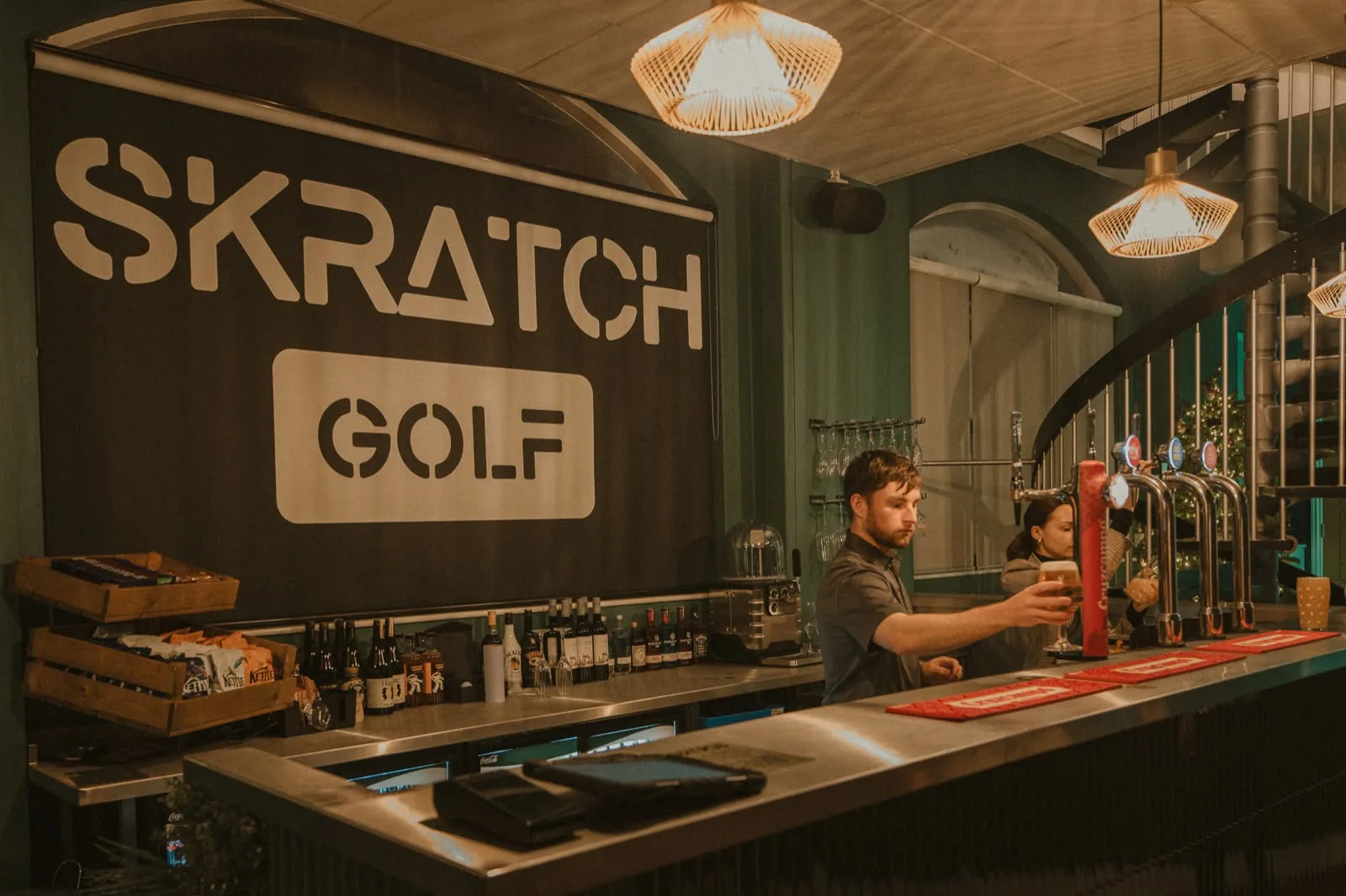 The SKRATCH Golf bar with the sign above and a bartender pouring a drink