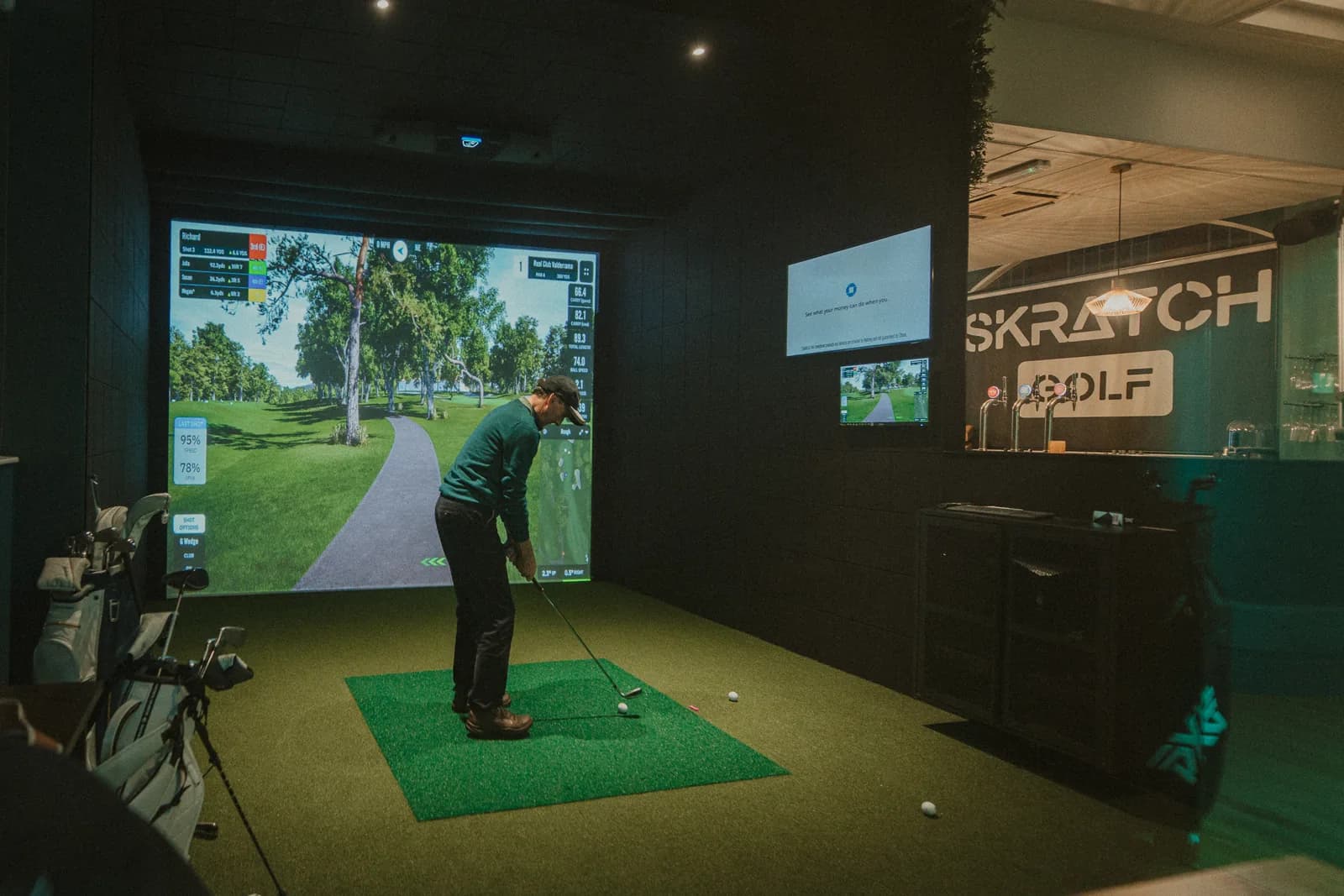 A wide view of a simulator bay with the SKRATCH GOLF sign on the wall