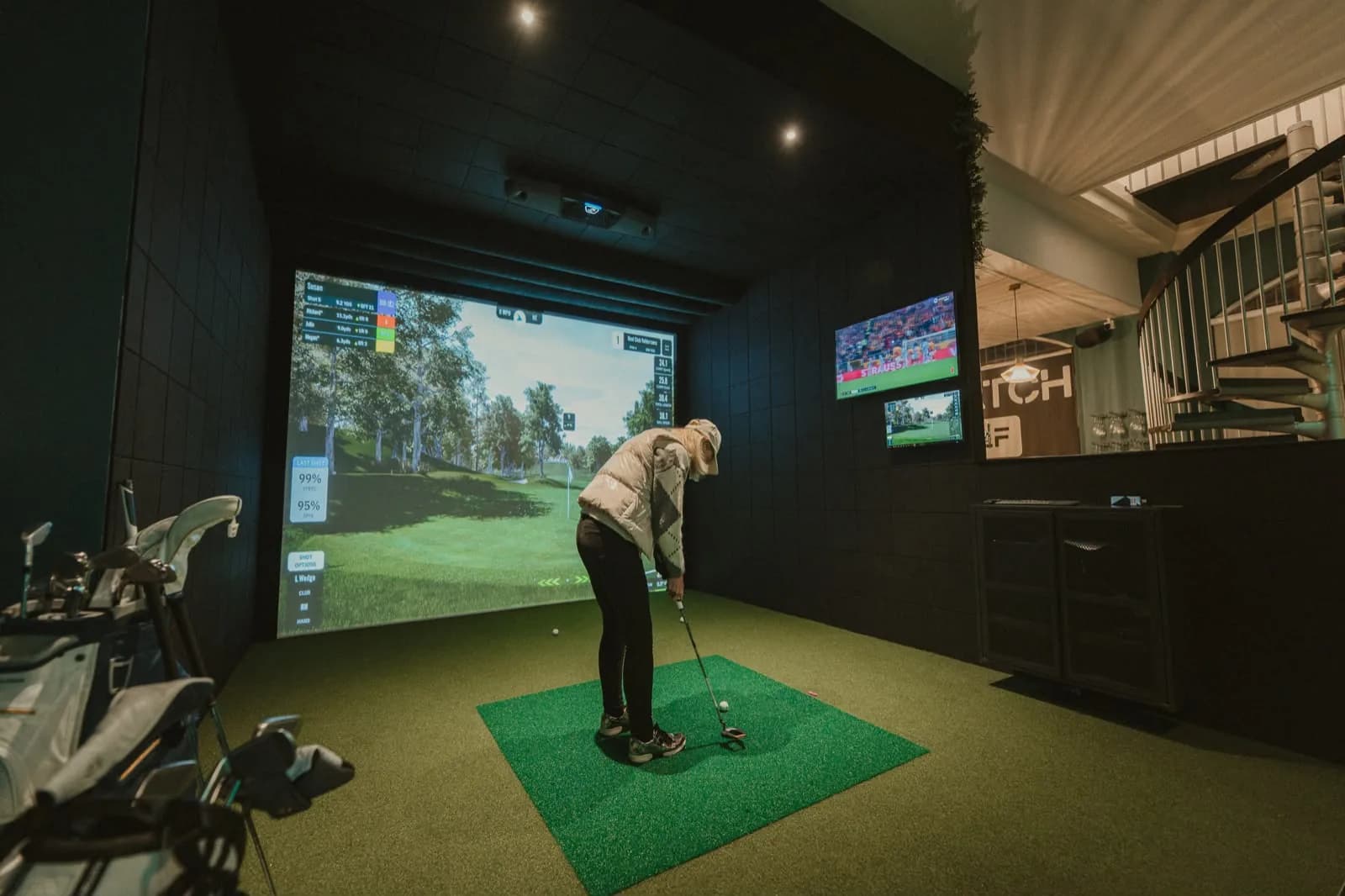A player lining up a putt in a simulator bay beside the spiral staircase