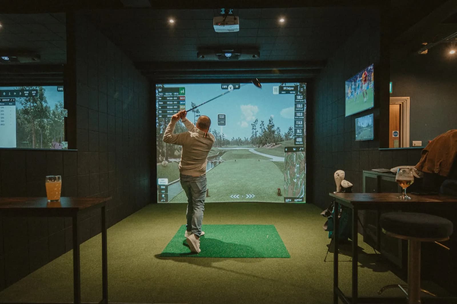 A player following through on a drive in a SKRATCH simulator bay, the course on the big screen