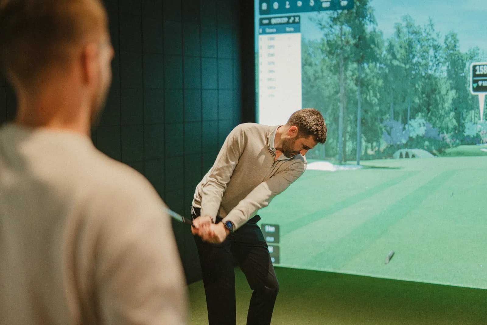 A coach watching a golfer's swing in a SKRATCH simulator bay