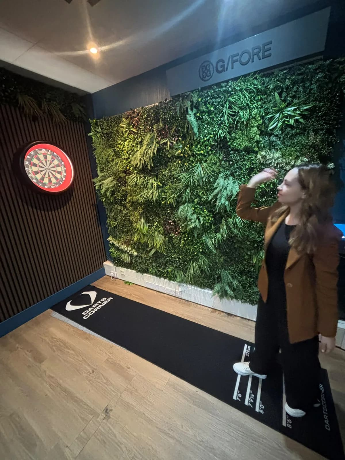 A guest throwing at the dartboard against the living green wall