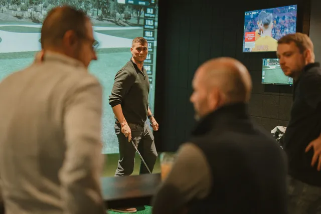 Members chatting over drinks while one plays in a simulator bay