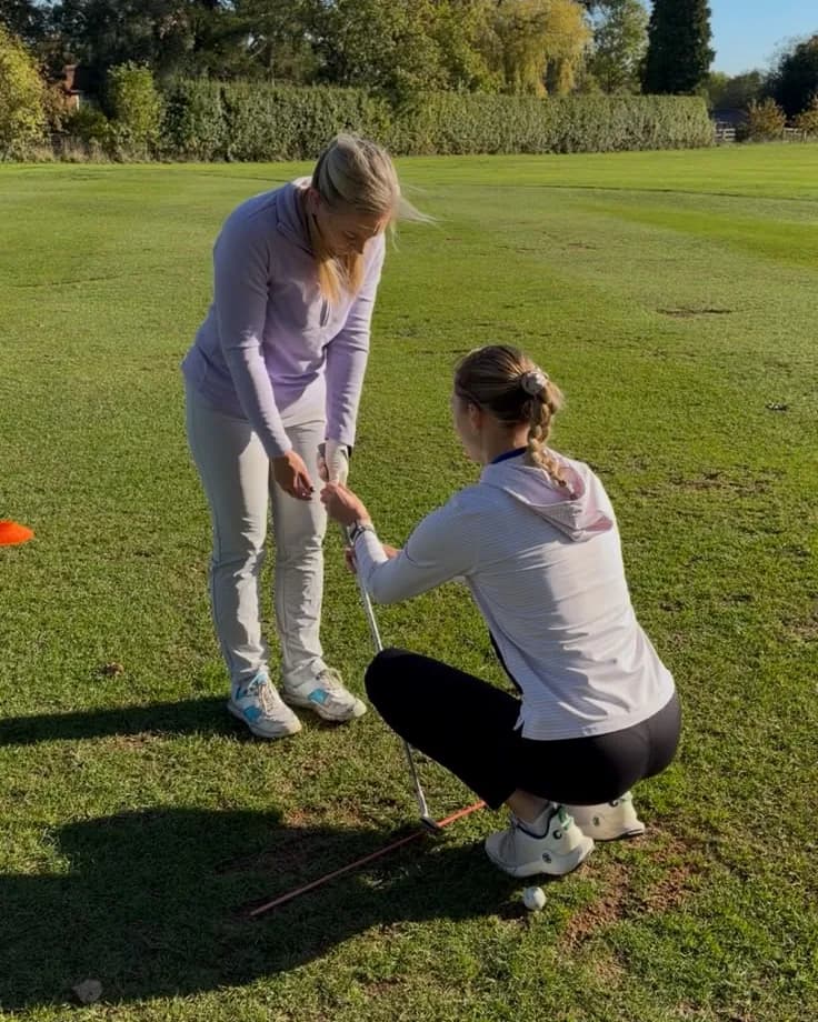 Two golfers on a practice ground, one adjusting the other's grip