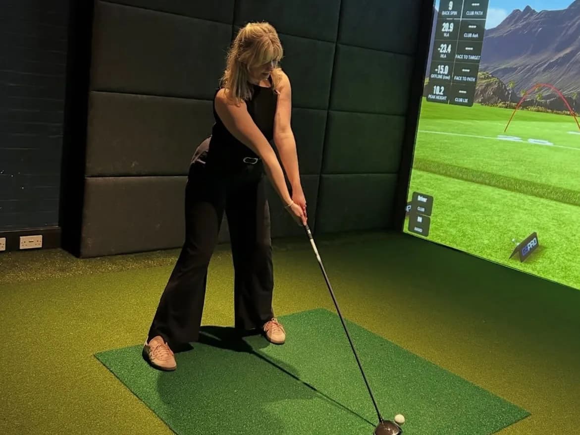 A woman lines up a drive on a SKRATCH simulator bay
