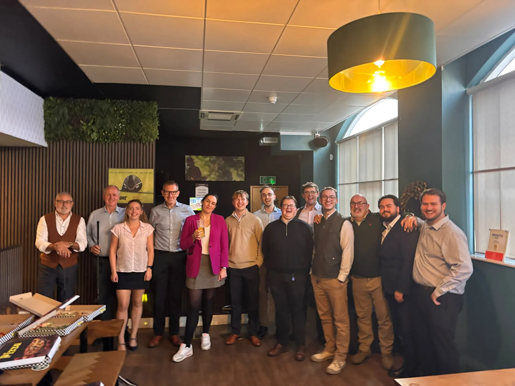 A work party group smiling together in the SKRATCH lounge, pizza boxes on the table